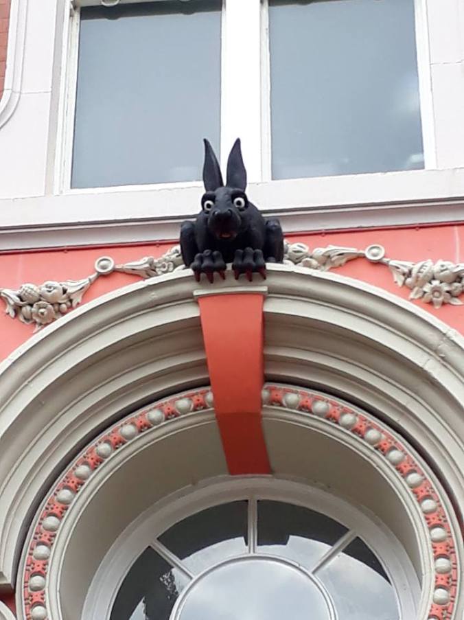 A black rabbit sculpture sits above an ornate white and pink door frame. He has blood-red nails and teeth!