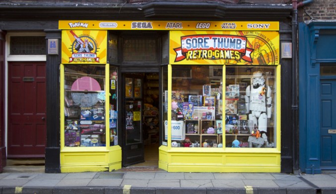 Frontage of Sore THumbs Retro Games, the window is jam packed with games and a life size Stormtrooper.